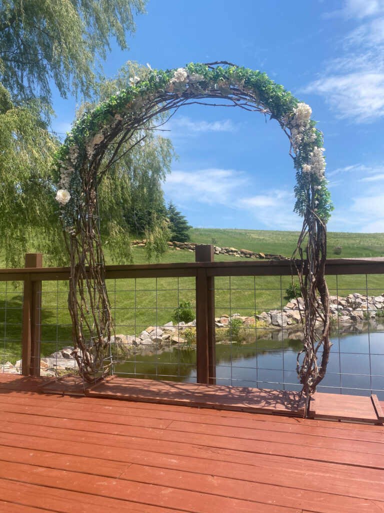 Arch-shaped arbor with faux florals on patio with pond in the background